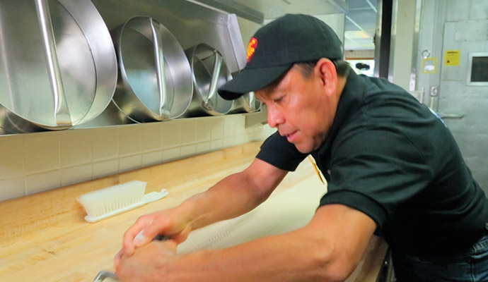Employee rolling out pizza dough